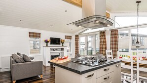 Une cuisine moderne dotée d’un îlot central, d’un coin repas avec des meubles blancs et d’un espace salon confortable avec un canapé gris.