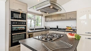 Une cuisine moderne dotée d’appareils électroménagers intégrés, d’un grand îlot central et offrant une vue sur l’extérieur.