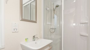 A bathroom with a white sink, a mirror, a shower enclosure, and a wall-mounted electrical outlet. - 2 bedroom accommodation in Talacre, Holywell (Talacre, Holywell)