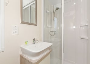 A bathroom with a white sink, a mirror, a shower enclosure, and a wall-mounted electrical outlet. - 2 bedroom accommodation in Talacre, Holywell (Talacre, Holywell)