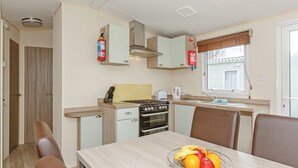 A compact kitchen with a stove, oven, and a small dining area with a table and chairs. - 2 bedroom accommodation in Talacre, Holywell (Talacre, Holywell)