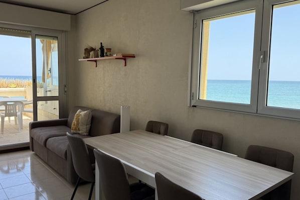 Una habitación con una mesa de comedor, sillas, un sofá, una puerta corrediza de vidrio que da a un balcón y un estante con adornos.