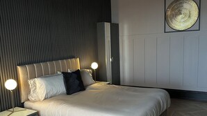 A modern bedroom with a large bed, bedside tables, a wall-mounted fan, and a decorative wall piece.