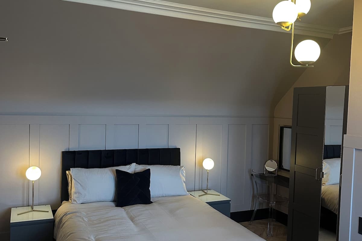 A neatly arranged bedroom with a large bed, two bedside tables with lamps, a mirror, and a wardrobe.