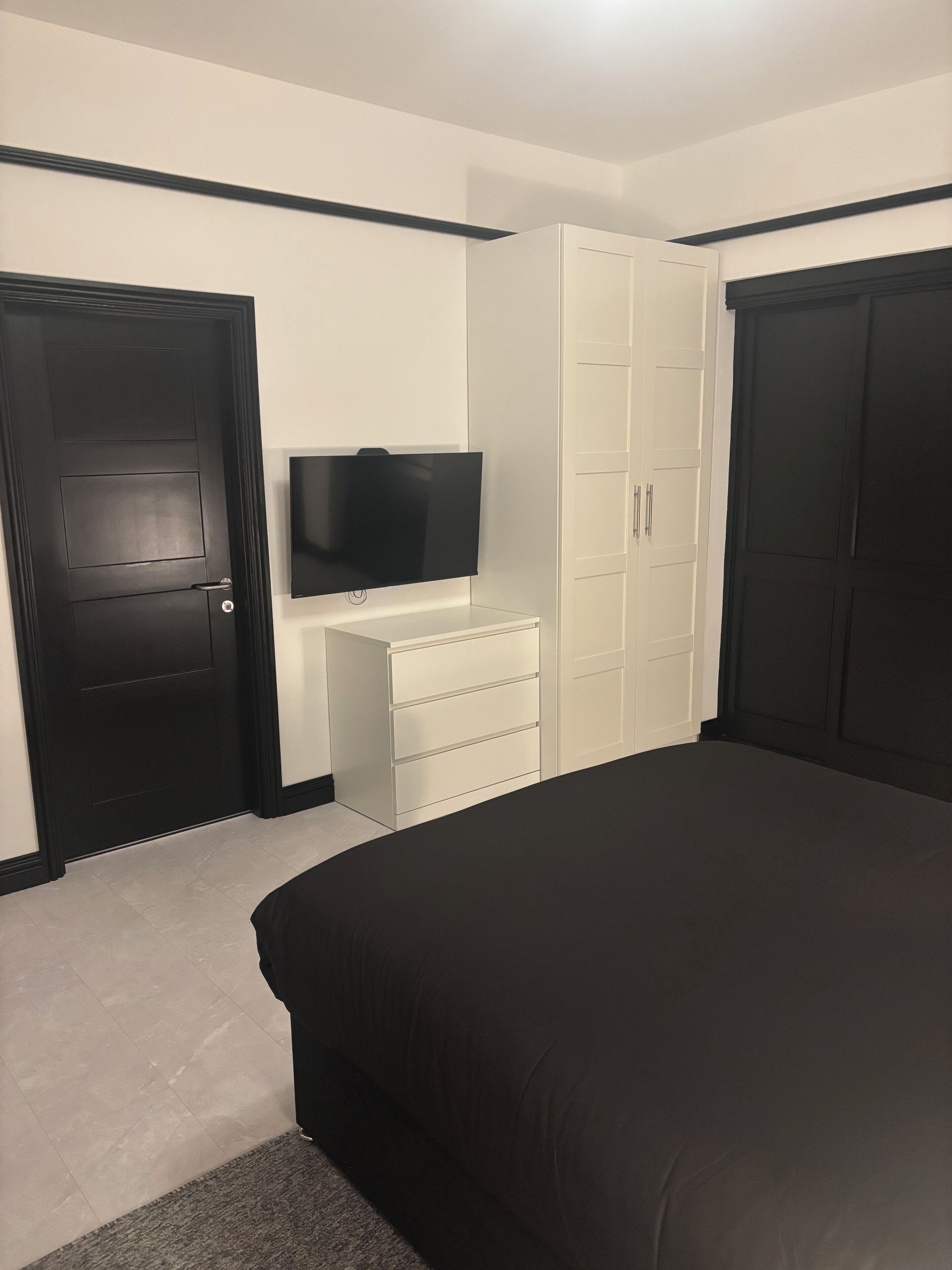 A bedroom with a large bed, a TV on a dresser, and two wardrobes.