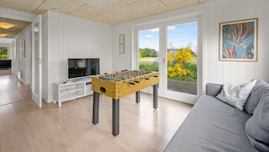 Ein geräumiges Wohnzimmer mit einem Kicker, einem Fernseher und einem Sofa.