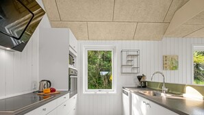 Eine moderne Küche mit weißen Schränken, einem eingebauten Backofen, einem Geschirrspüler und einem Fenster mit Blick auf Grünflächen.
