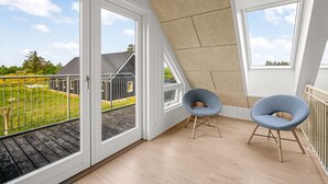 Ein geräumiges Dachzimmer mit großen Fenstern, Holzboden und zwei blauen Stühlen.