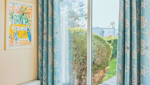 A room with a large window, blue curtains with a leaf pattern, and a framed picture on the wall. - 3 bedroom accommodation in Talacre, Holywell (Talacre, Holywell)