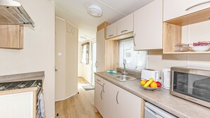 A compact kitchen with a stove, sink, and microwave. - 3 bedroom accommodation in Talacre, Holywell (Talacre, Holywell)