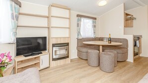 A compact living space with a flat-screen TV, a built-in fireplace, a round dining table with ottomans, and a kitchenette area. - 3 bedroom accommodation in Talacre, Holywell (Talacre, Holywell)