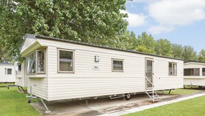 A single-story mobile home with a front porch, a small attached garage, and a designated parking space. - 3 bedroom accommodation in Talacre, Holywell (Talacre, Holywell)