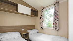 A small, single-room accommodation with two beds, a window with curtains, and built-in shelves. - 3 bedroom accommodation in Talacre, Holywell (Talacre, Holywell)