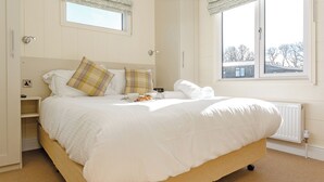 A bedroom with a large bed, two bedside tables, a window with a view, and a radiator. - 4 bedroom accommodation in Axminster (Axminster)