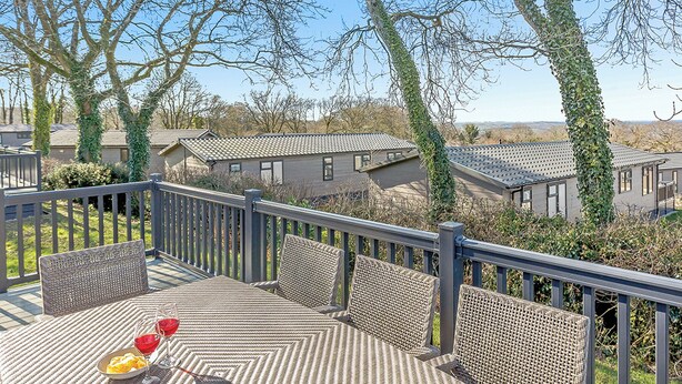 A deck with wicker furniture and a table, overlooking a residential area with houses and trees. - 4 bedroom accommodation in Axminster (Axminster)