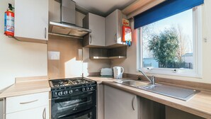 A compact kitchen with a gas stove, oven, and a window with a view of trees. - 3 bedroom accommodation in Talacre, Holywell (Talacre, Holywell)