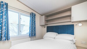 A bedroom with a bed, a window with curtains, a headboard, and built-in shelving. - 3 bedroom accommodation in Talacre, Holywell (Talacre, Holywell)