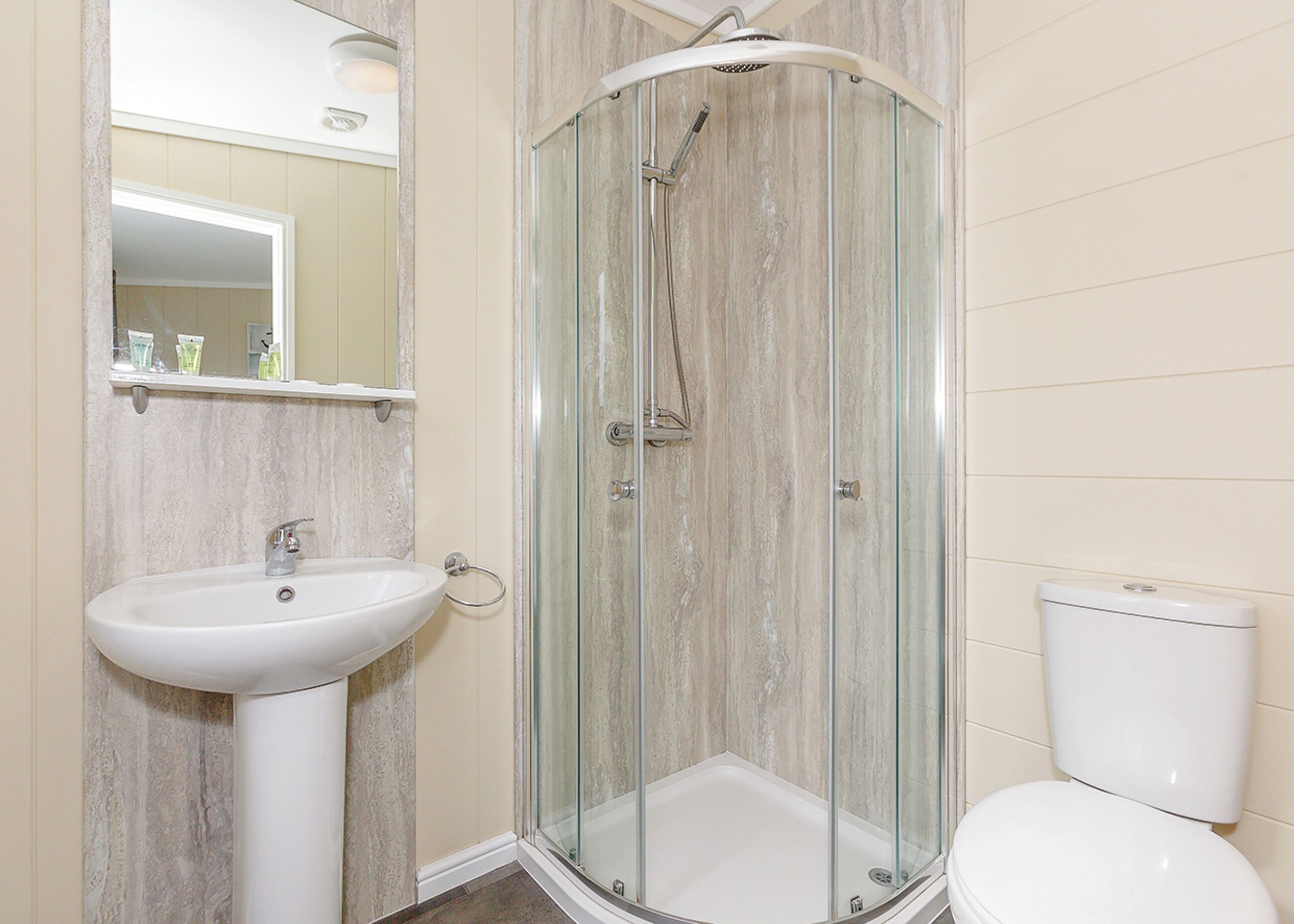Un baño con cabina de ducha de vidrio, lavamanos pedestal y retrete.