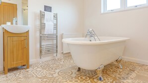A bathroom with a freestanding bathtub, a wooden cabinet, a towel rack, and patterned floor tiles.