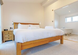 Une chambre à coucher avec un lit en bois, une table de chevet, un bureau intégré, une fenêtre et une baignoire.