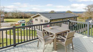 A deck with outdoor furniture, a view of a house, and a car parked outside. - Fresh and contemporary styled lodge. (Axminster)