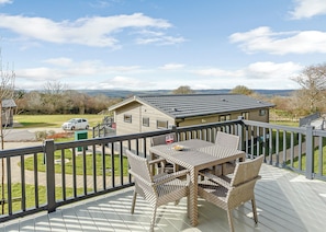 A deck with outdoor furniture, a view of a house, and a car parked outside.