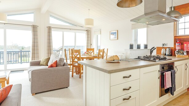 A modern kitchen with a central island, dining area with chairs, and a sofa. - Fresh and contemporary styled lodge. (Axminster)