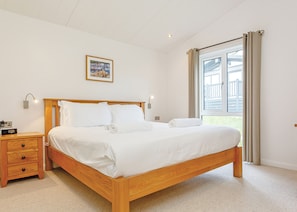 A bedroom with a wooden bed, a nightstand, a wall-mounted lamp, and a window with curtains.