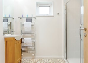 A bathroom with a sink, mirror, towel rack, and shower.