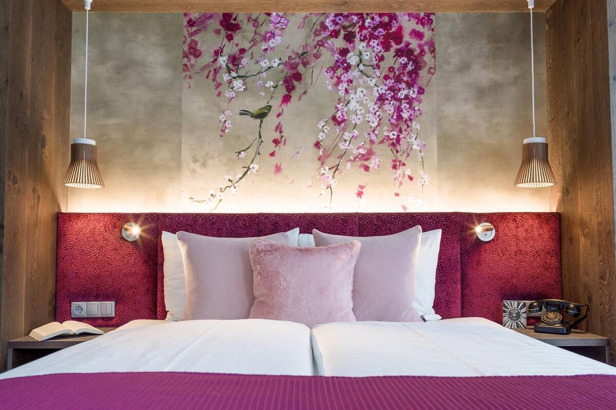 A bedroom with a large bed, a red textured headboard, and a wall-mounted artwork of pink flowers.