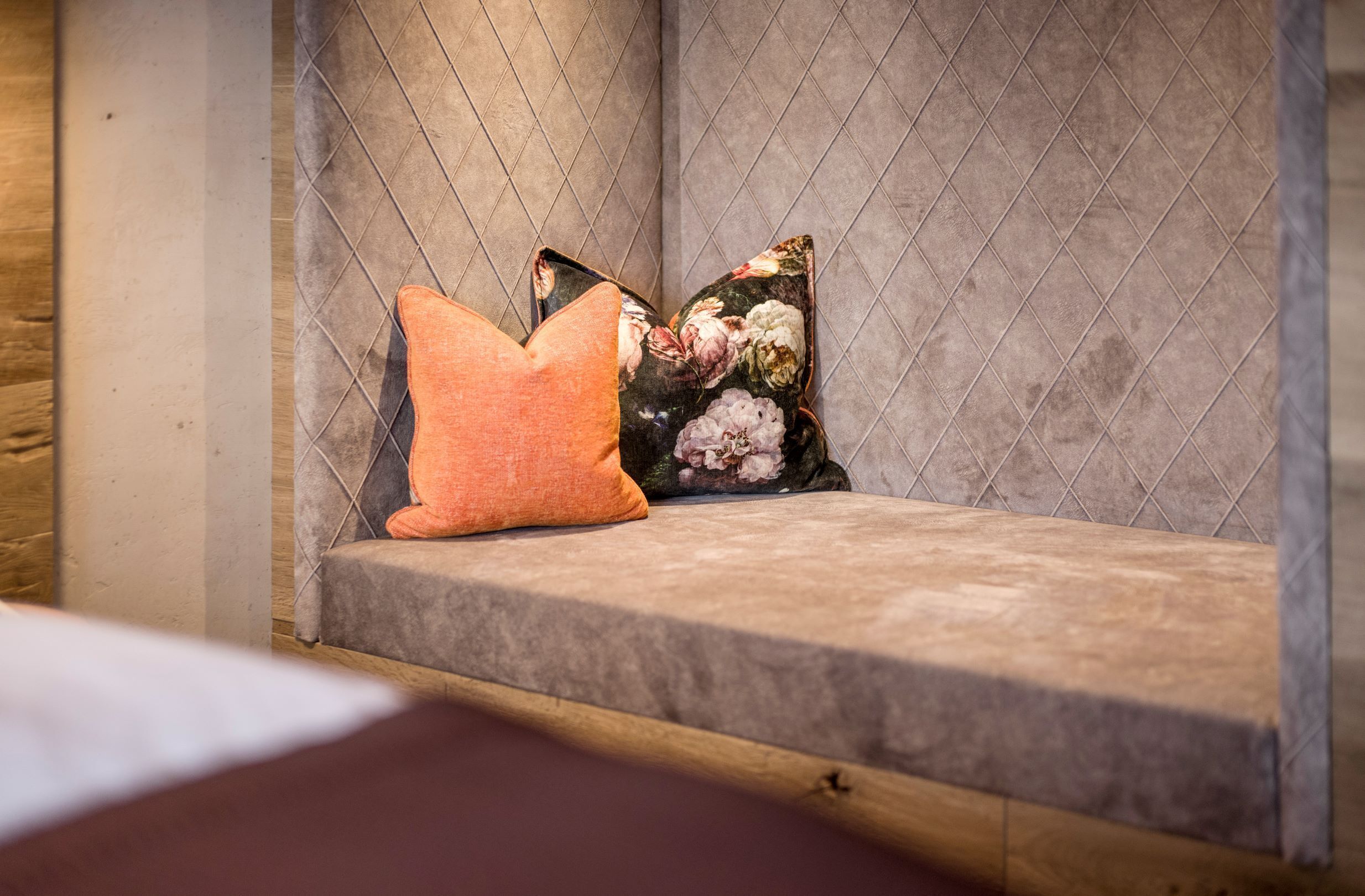 Un banco con cojín y almohada estampada frente a una pared con textura.