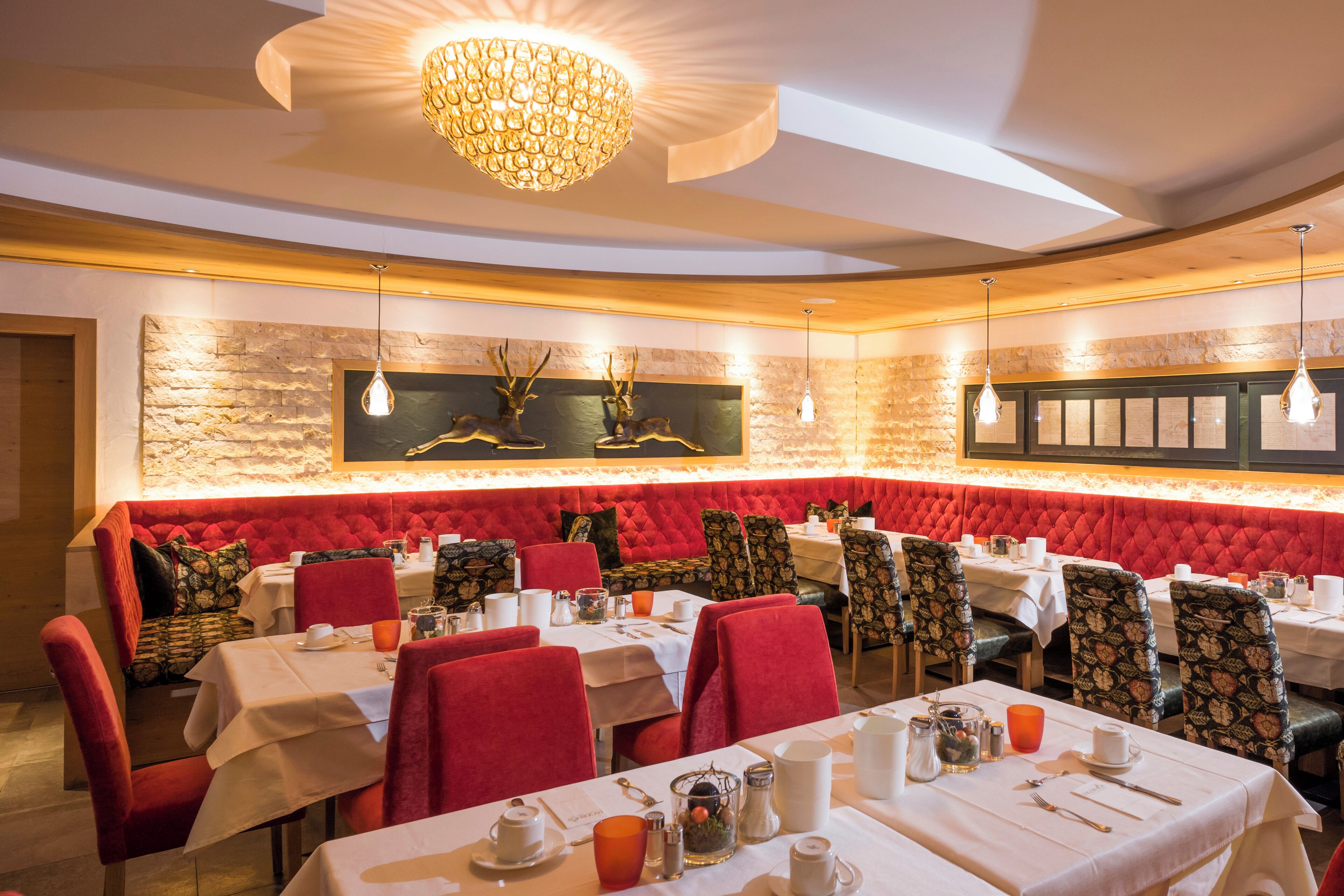 A restaurant with red upholstered booths, white tablecloths, and a stone accent wall.