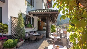 An outdoor patio area with tables and chairs, surrounded by potted plants and a wooden fence. - Hotel Jägerhof (Mayrhofen)