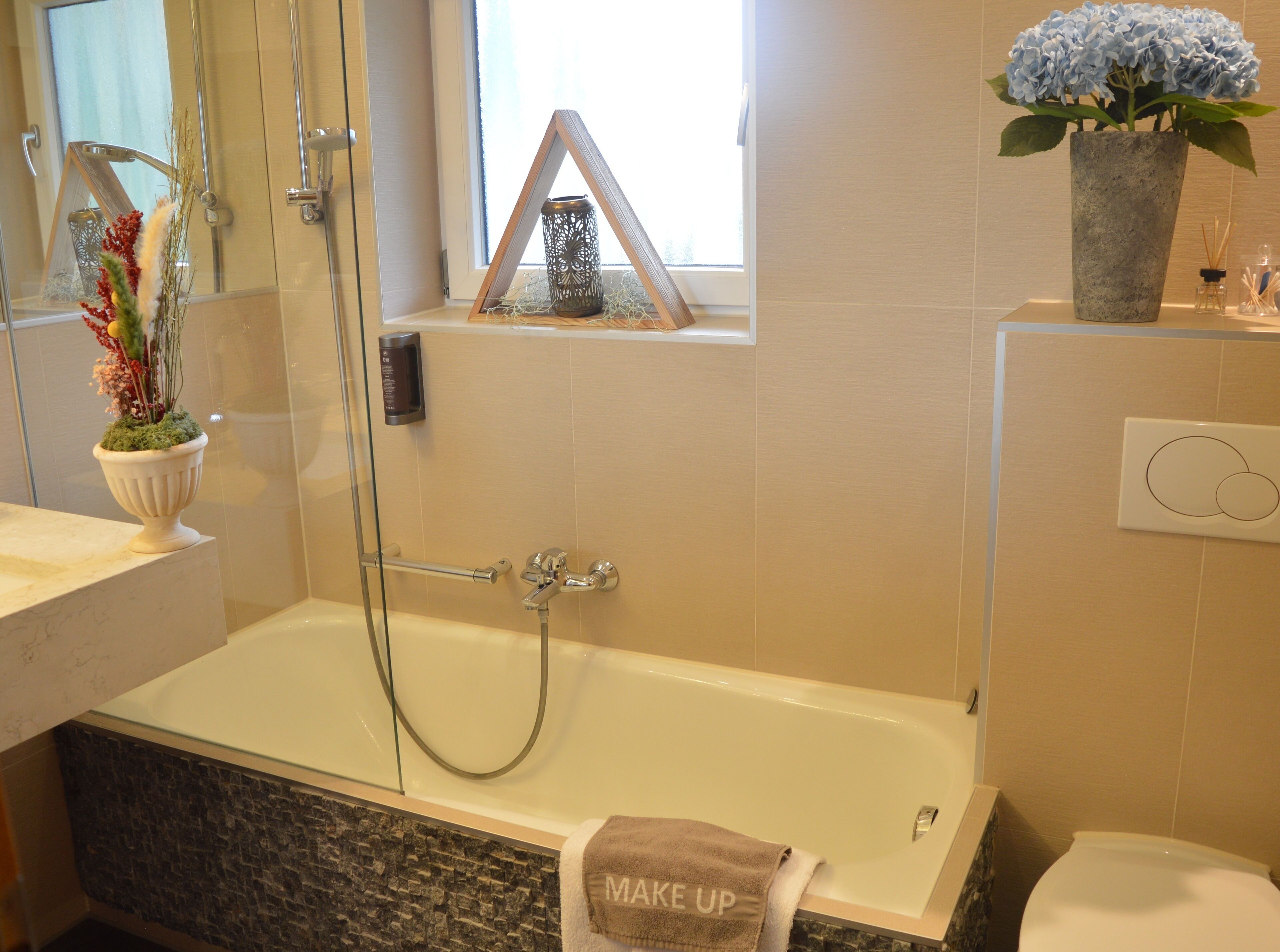 A modern bathroom with a bathtub, a glass shower enclosure, a window with a view, a towel rack with a towel, and a potted plant.