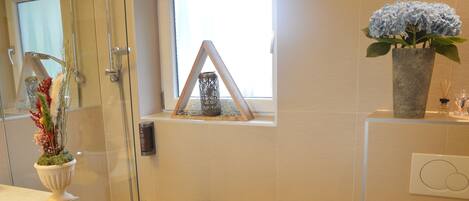 A modern bathroom with a bathtub, a glass shower enclosure, a window with a view, a towel rack with a towel, and a potted plant.