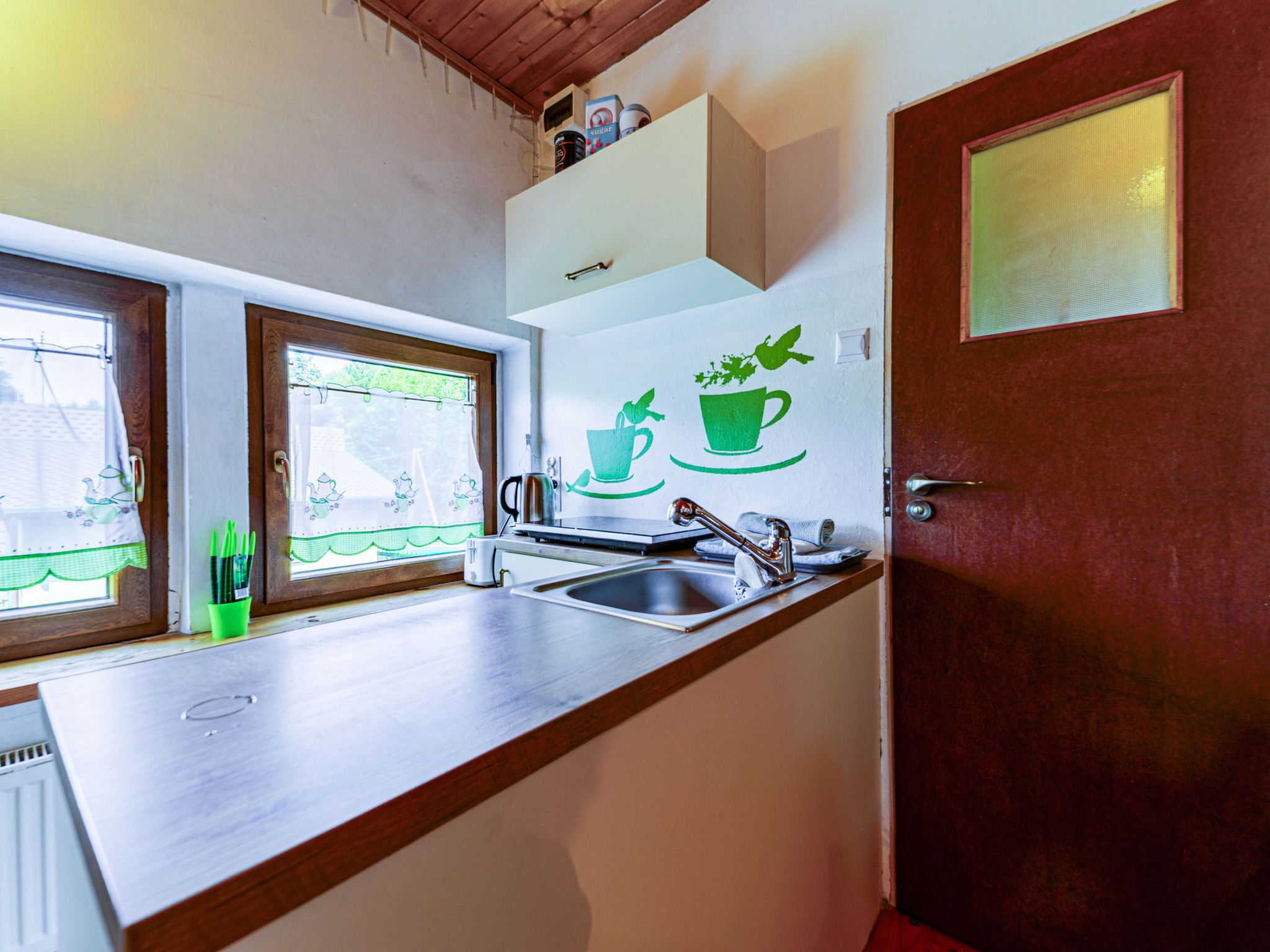 A kitchen with a wooden countertop, a sink, and a window with a view of greenery. There is a door with a glass panel and a shelf above the counter.