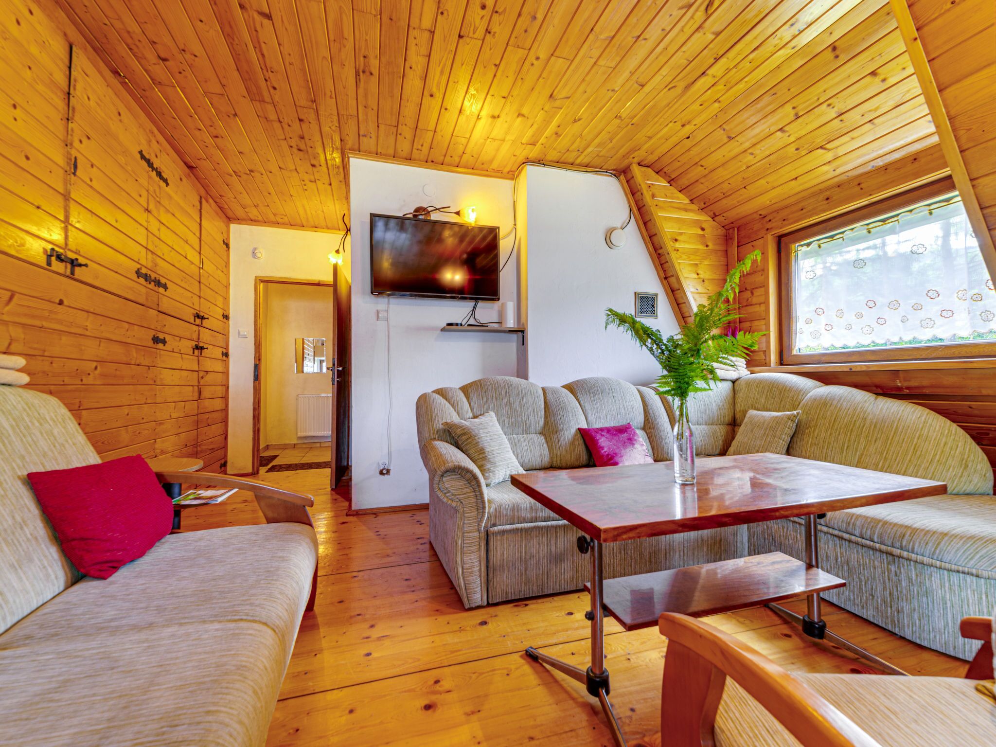 Interior acolhedor de uma cabana com paredes e assoalhos de madeira, um sofá, uma mesa e uma televisão montada na parede.