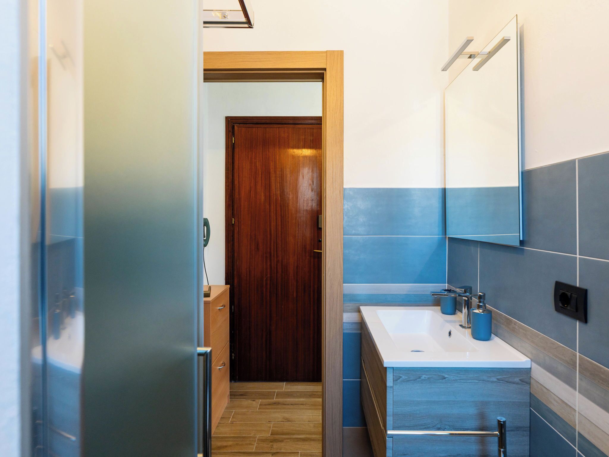 A modern bathroom with a wooden door, a white sink, and blue-tiled walls.