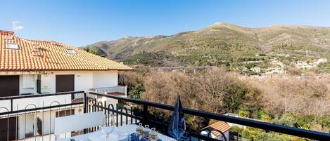 A balcony with a table set for two, overlooking a mountainous landscape with a clear sky.