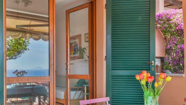A dining area with a table set for two, a view of the sea, and a balcony with a chair. - Sunny House by Interhome (Marina di Campo)