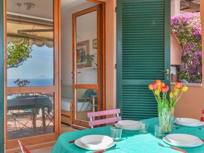 A dining area with a table set for two, a view of the sea, and a balcony with a chair. - Sunny House by Interhome (Marina di Campo)