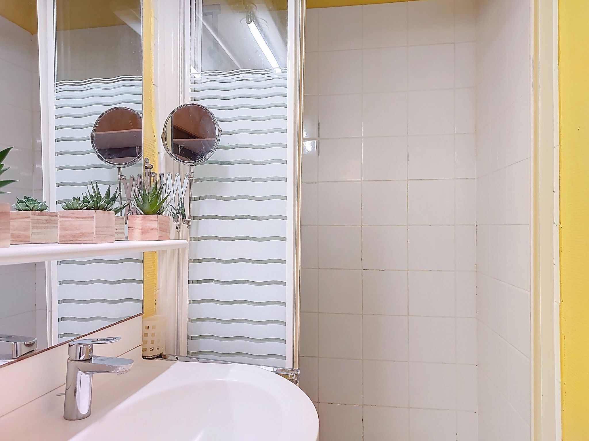 A bathroom with a white sink, two round mirrors, and a tiled shower area.