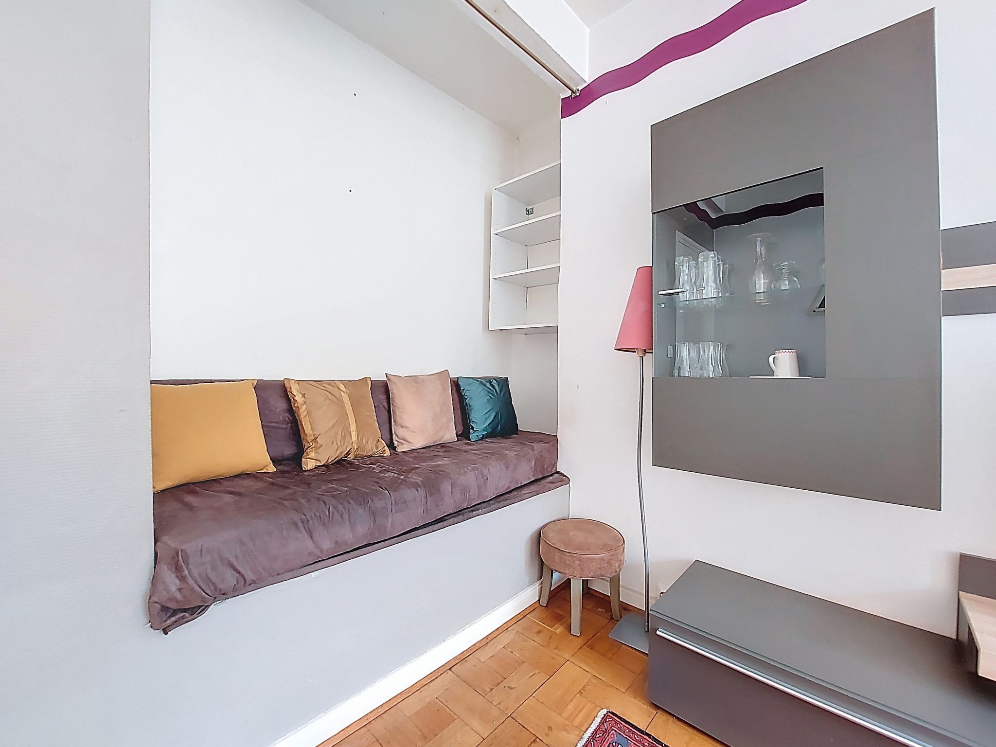 A modern living room with a sofa, a small stool, a cabinet, and a mirror.