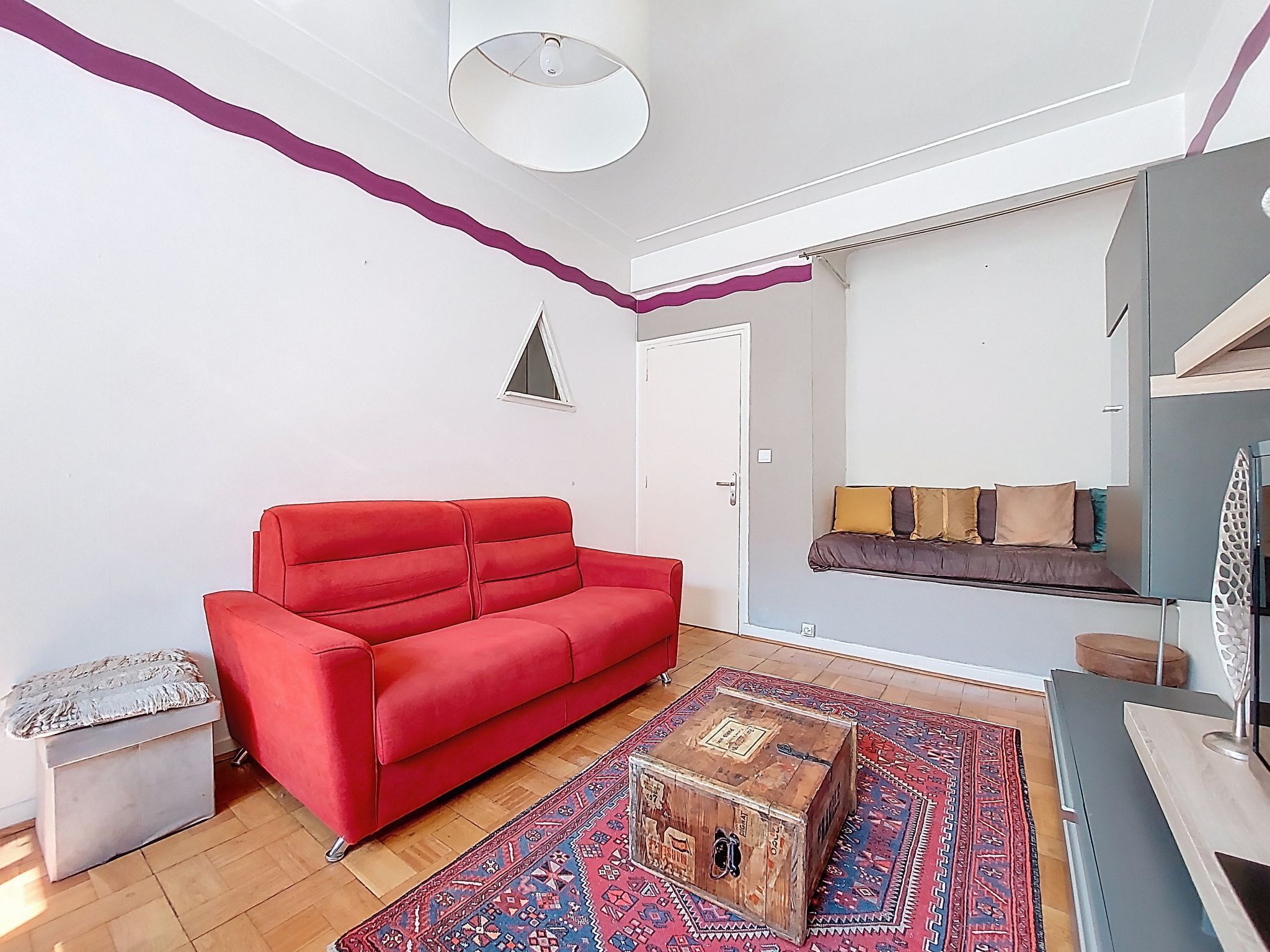 Een moderne woonkamer met een rode bank, een kamerkleed met patroon en een houten dressoir.