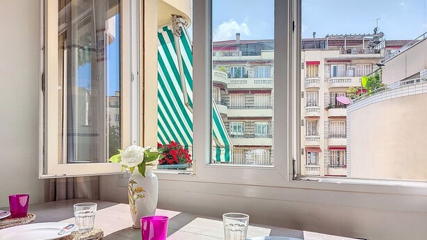 A dining table set with plates, cutlery, and glasses, with a view of a residential building through a window. - Apartment Daphné by Interhome (Nice)
