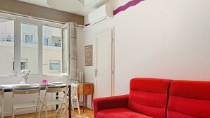 A room with a red sofa, a dining table with chairs, and a window with curtains. - Apartment Daphné by Interhome (Nice)