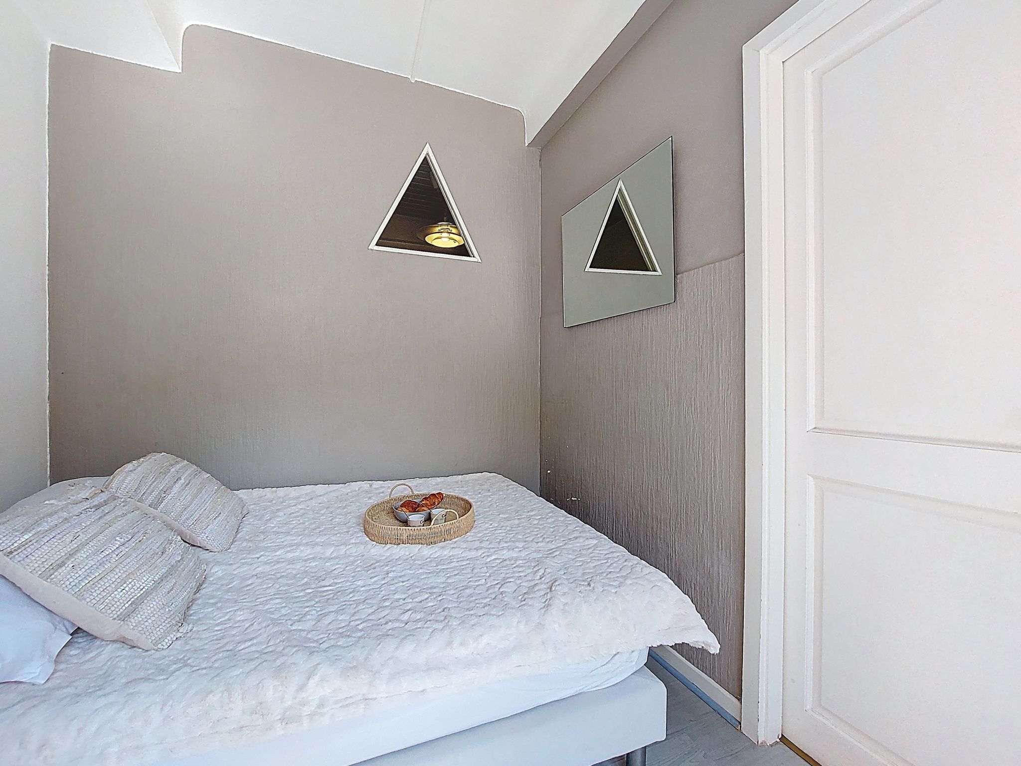 Une chambre à coucher avec un lit, une table de chevet sur laquelle se trouve un panier, et deux miroirs fixés au mur.