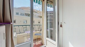 A balcony with a glass door, outdoor furniture, and a view of neighboring buildings. - Apartment Daphné by Interhome (Nice)