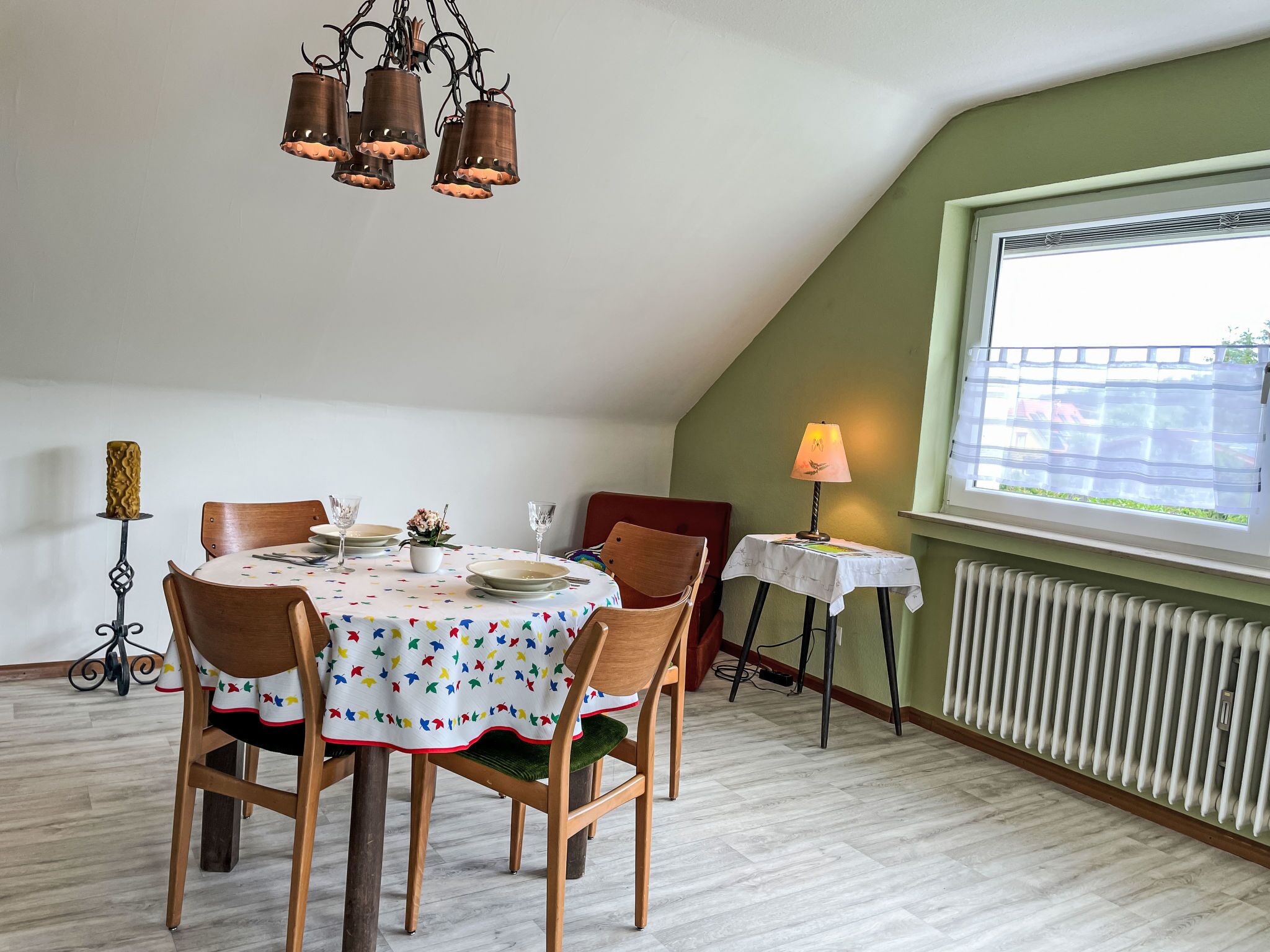 A dining area with a round table set for four, a window with blinds, a radiator, and a lamp on a side table.