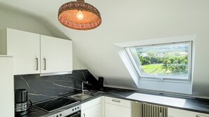 Eine moderne Küche mit weißen Schränken, einer schwarzen Arbeitsplatte, einem eingebauten Ofen, einer Kaffeemaschine und einem Fenster mit Blick auf Grünflächen.